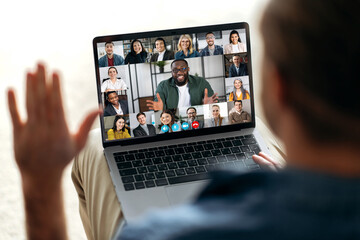 Fototapeta na wymiar Online video communication concept. Over shoulder view at a laptop screen with different people, employees, business partners, guy greets colleagues, online briefing, brainstorming, group teleworking