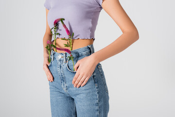 cropped view of young woman in jeans with lupine flowers in pockets posing isolated on white