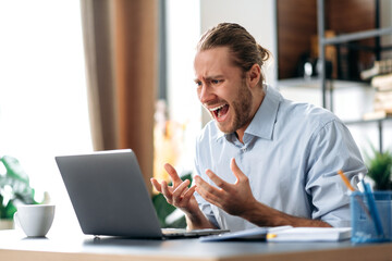 Fototapeta premium Shocked annoyed caucasian busy guy looking at a laptop in confusion, received unexpected news, failed a deal, shouts, gesturing with hands, sitting at the work desk at home office