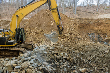 Excavator clearing rock and soil for new road construction site