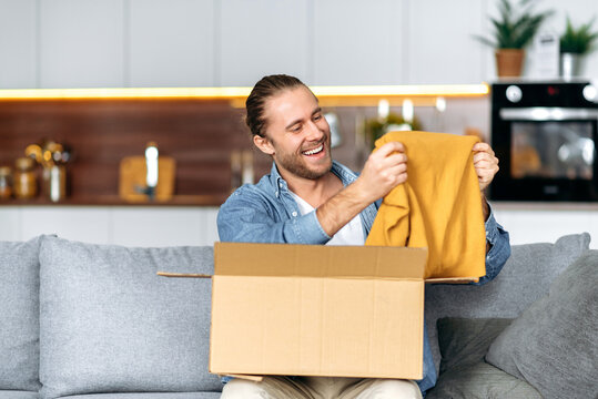 Smiling attractive man unpacked his parcel, happy about getting a long expected order. Caucasian modern guy shopping in internet stores, buying new clothes online, online shopping concept