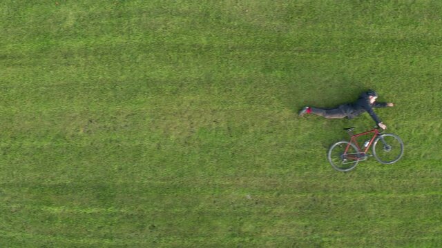 Cyclist lies on a green lawn with a bike in a super hero pose. Top aerial view.