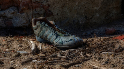 Old worn-out shoe with worn leather and no laces in an abandoned house. There is a pile of garbage around, the background is a wall of red stone and clay.