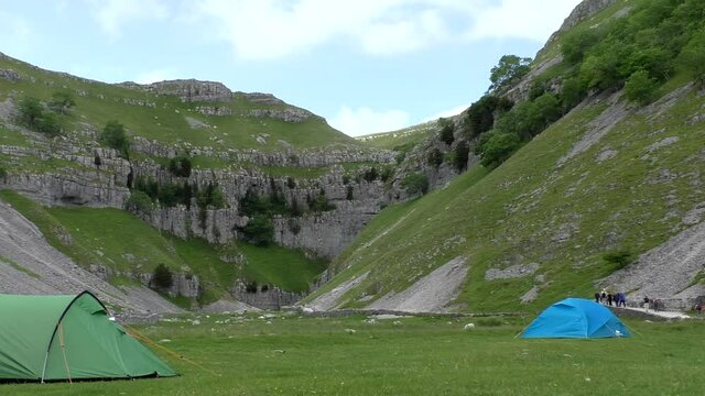 Camping site at Malham Cove, distant people walking on the footpath towards waterfalls.