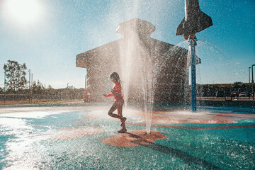 Cute adorable Caucasian funny girl playing on splash pad playground on summer day. Seasonal water sport recreational activity for kids outdoors. - Powered by Adobe