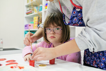 Girl with Down syndrome in glasses draws with the help of a volunteer