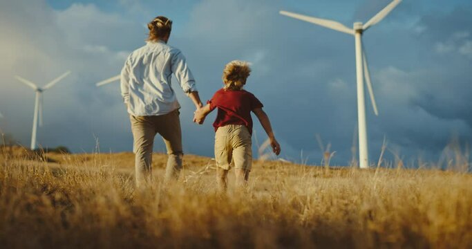 Father and son walking to windmills on golden hill at sunset, family lifestyle, clean energy wind turbines, future generations and clean sustainable energy