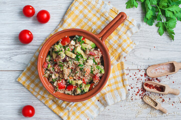 Delicious quinoa salad with avocado, cucumber and tomatoes on a rustic wooden table. Superfoods concept. Selective focus. View from above.