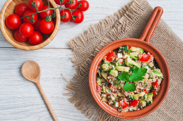 Delicious quinoa salad with avocado, cucumber and tomatoes on a rustic wooden table. Superfoods concept. Selective focus. View from above.