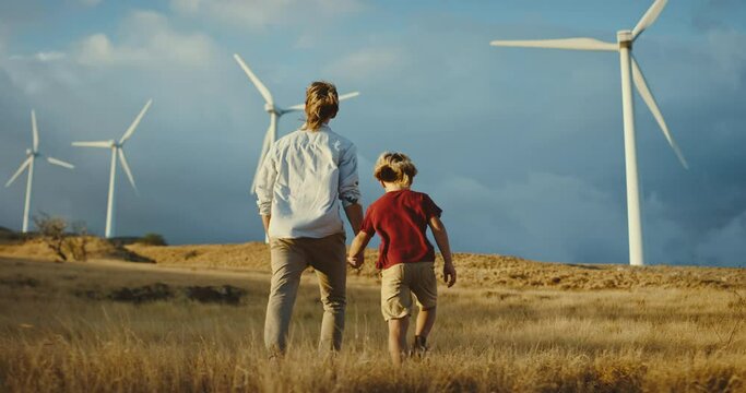 Father and son walking towards white windmills on a golden hill at sunset, walking to a cleaner and promising future, sustainability for future generations, father and son family lifestyle