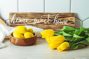 Home sweet home handwritten sign on kitchen countertop next to wooden bowl with yellow Easter eggs and tulip bouquet
