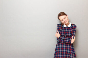 Portrait of happy girl hugging herself and smiling with closed eyes