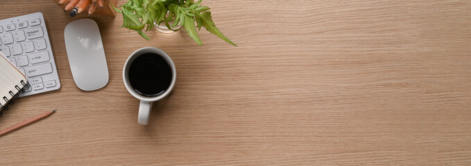 Horizontal image of office desk with coffee cup, plant, notebook and copy space on wooden background.