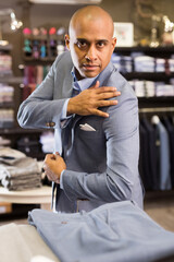 Fototapeta na wymiar Focused man deciding on suit jacket while shopping at apparel shop
