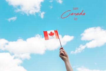 Happy Canada Day. Greeting card with text. Human hand arm waving Canadian flag against blue sky. Proud citizen man celebrating national Canada Day on 1st of July outdoors.