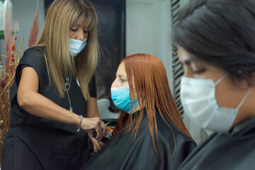 Client with a mask in the hairdresser salon with social distancing against covid-19. Caucasian lady with red hair at the stylist.