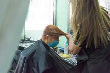 hairstylist with mask cutting her client's wet red hair. Women in Hairdresser salon. 