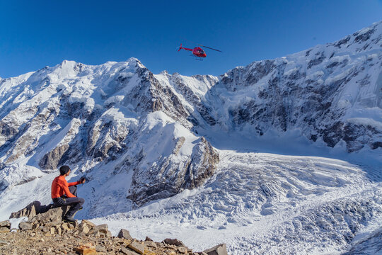 A beautiful landscape with mountains, a huge blue glacier and a middle-aged mountaineer sitting with a walkie-talkie in his hands calls the rescue service waiting for an ambulance helicopter