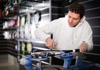 Diligent serious male master is pulling racket for tennis in the store.