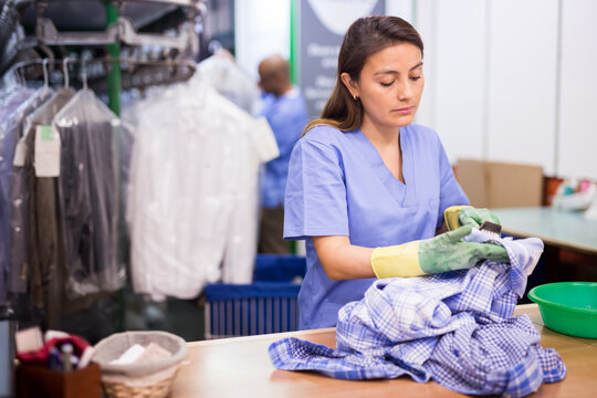 Portrait of confident dry cleaning employee at work, woman cleaning shirt with brush
