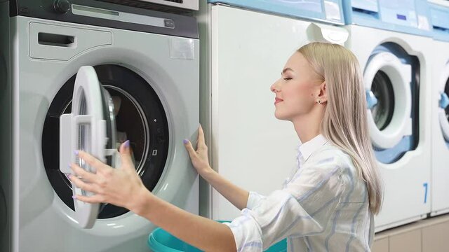 An attractive woman picks up laundry from a washing machine in a public laundry room. Self-service laundry. slow-motion