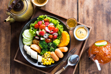 Homemade fruit vegetable salad, honey mustard, tomato,strawberry,orange,apple,banana,maize and sausage in bowl  with lemon tea on wooden background.Top view.Selective focus.