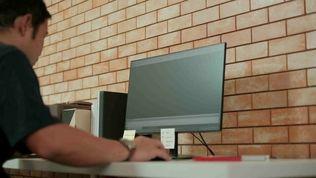 An Asian architect in a dark shirt is drafting the construction plan by using computer-aided design program in his desktop computer.