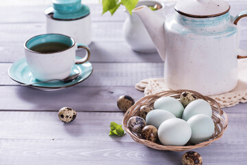 Easter composition with painted blue eggs, a cup of tea and spring tree branches with green leaves on a white background. Selective focus.