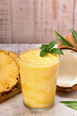 pineapple coconut smoothie with a mint leaf on top. on the side pineapple slices and two coconuts. stone surface and white wooden planks background. copy space for advertising.