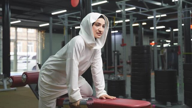 muslim woman in hijab for sports exercises with dumbbells in the gym, woman focused on training, sports, fitness, workout concept.