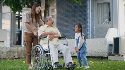 Disabled senior grandpa on wheelchair with grandchild and mother in park, Happy Asian three generation family having fun together outdoors backyard, Grandpa and little child smiling and laughed