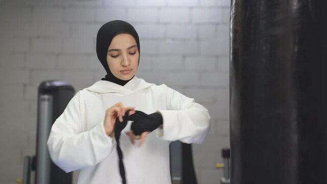 strong Muslim woman prepares for training, boxing alone in the gym, woman ties Ricky elastic bandages.