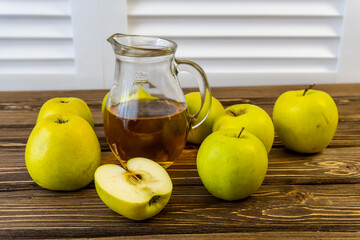 Green apples and jug with apple juice on wooden background