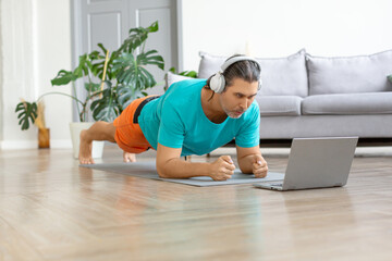 Photo of a middle-aged man in headphones doing the plank exercise. He follows the online tutorial from internet.