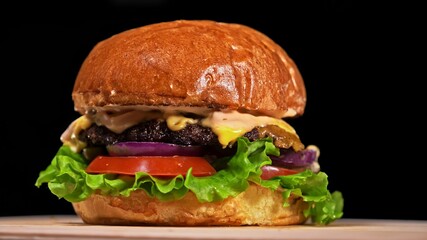 Craft burger is cooking on black background in black food gloves. Consist: sauce, lettuce, tomato,...