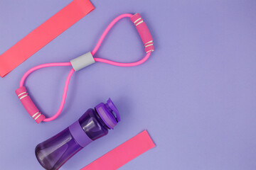 Fitness clothes and accessories for woman on violet background. Sports fashion  with  t-shirt, elastic bands, headphones, phone, bottle. Healthy, active  lifestyle concept