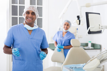 Portrait of professional male dentist in office with dental assistant background