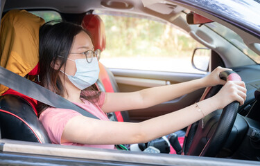 Young Asian woman wearing surgical mask for prevent the spread of coronavirus while driving car.