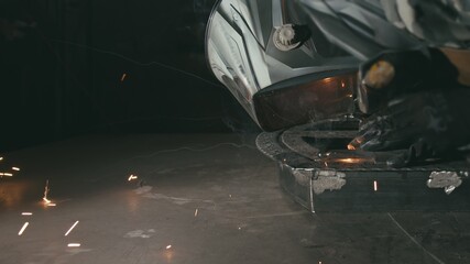 Forge workshop. Smithy. Worker in a welding hood helmet welds a part by electric welding. Sparks...