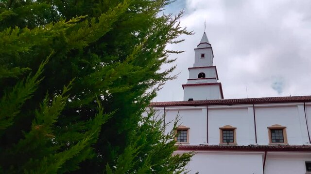 White church behind a green tree on top of the Monserrate cable car in Bogotá, Colombia.