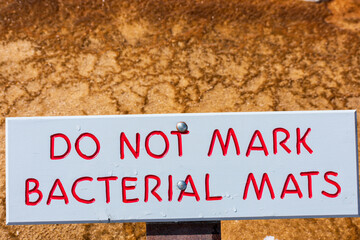 Do Not Mark Bacterial Mats sign in Yellowstone National Park reminds tourists not to deface the environment. Background orange thermophilic bacteria mats.