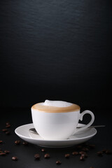 White cup of cappuccino on a black textured background. Italian cappuccino. Morning coffee in Italy. Coffee on black. Coffee beans. Close-up on a white cup.
