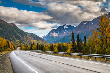 road trip on open highways traversing jagged snow capped mountain peaks and vibrant autumn foliage of the trees in wild Alaska.