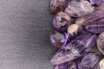 Rutilated amethyst jewel heap on black stone half background. Pile mineral pebbles texture. Place...