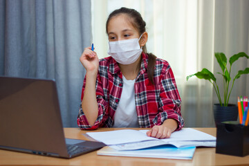 A brunette girl in a medical mask, dressed in a red shirt sitting at home studying, doing homework, communicates online. - Powered by Adobe