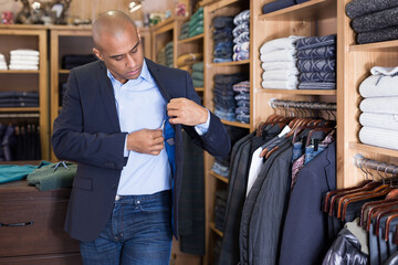 Confident young man looking for jacket in mens clothing boutique