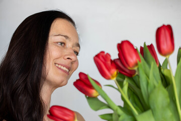 Spring holidays, International womans day, 8 march, mothers or valentines day celebration. Middle aged pretty woman smiling, holding and admiring bouquet of red tulips, studio portrait. Copy space