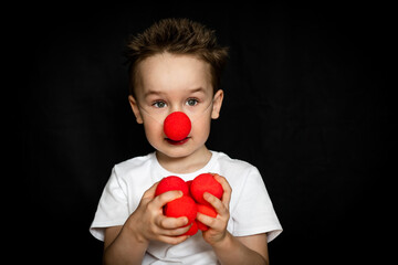 Boy with a clown red nose and red noses in his hands. Red Nose Day.