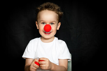 Boy with a clown red nose and red noses in his hands. Red Nose Day.