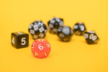 Red D20 dice on a yellow background and group of black dices D30, D12, D10 and D8: space for text, side view, concept of role-playing games and games for the whole family at home